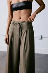 Pantalón culotte de tiro medio, con diseño de pierna ancha y pliegues frontales. Cuenta con cintura ajustable mediante cordones, bolsillos laterales y cierre frontal con cremallera y gancho metálico.