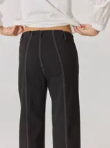 Pantalón de corte relajado color marrón, confeccionado en una mezcla de algodón y elastano. Presenta costuras en contraste color rojo en bolsillos y bragueta, con cierre de botón metálico.