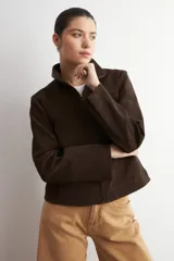 Chaqueta de cuero color marrón oscuro, con cuello alto, cierre frontal y diseño minimalista de corte recto.