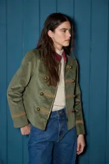 Blazer corto de estilo militar confeccionado en terciopelo azul marino, con cuello mao, cierre frontal con cremallera, detalles de galones bordados y botones metálicos decorativos.