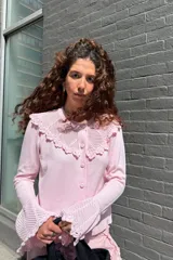 Saco de punto color rosado con mangas largas, cierre frontal de botones y detalles de tejido calado en el cuello y los puños acampanados.