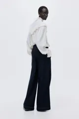 Pantalón de jean de tiro alto con pierna amplia y corte holgado. Confeccionado en denim rígido de color azul oscuro, presenta costuras decorativas verticales en el frente, bolsillos laterales y un cinturón integrado del mismo material con hebilla.
