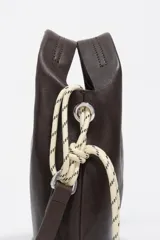 Bolso tipo bucket de cuero negro con asa de mano, tiras decorativas laterales y el logo impreso en plateado en el frente.