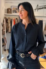Camisa negra de manga larga con detalles de broderie y calados en el frente. Presenta cuello mao, cierre frontal con botones y puños con volados.