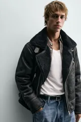 Cazadora de estilo biker con exterior de efecto cuero y forro interior de borreguillo. Presenta cierre frontal asimétrico con cremallera, cuello solapa con trabilla, bolsillos con cremallera y bajo ajustable con trabillas laterales.
