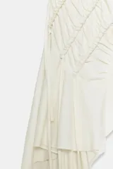 Top de algodón color crudo, con diseño sin mangas, cuello redondo y bajo asimétrico acabado en volante. Presenta frunces diagonales con detalles de cordones y cierre trasero con abertura y botón.