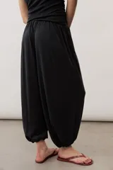 Pantalón holgado negro tipo bombacho, con cintura elástica y puños fruncidos en los tobillos.