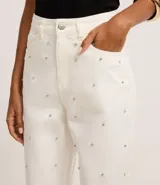 Pantalón mom comfort de cintura alta confeccionado en sarga color crudo, con trabillas en la cintura, cierre tradicional, bolsillos y brillo aplicado con lunares metalizados y pedrería de strass.