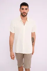 Camisa de manga corta color crudo, con cuello camisero y abotonadura frontal.