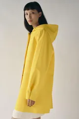 Cazadora impermeable de acabado engomado en color amarillo, con capucha ajustable, cierre frontal con botones a presión, bolsillos laterales y mangas largas ajustables.