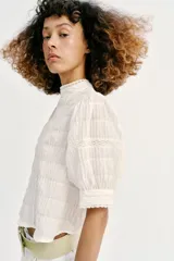 Camisa rosa de cuello alto, mangas cortas abullonadas y detalles de encaje y entredós en el frente y las mangas.