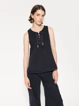 Top sin mangas de gabardina color azul oscuro, con escote redondo y detalle de cordón con ojalillos en el centro del pecho. Presenta recortes triangulares que generan vuelo en la parte inferior.