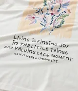 Remera de algodón color blanco crudo, manga corta y cuello redondo, con un pequeño estampado floral y lettering en el área del pecho.