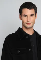 Sobrecamisa negra de pana con cuello clásico, cierre frontal con botones, dos bolsillos de parche con solapa en el pecho y puños abotonados.