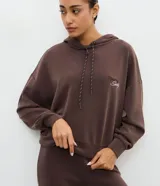 Buzo deportivo con capucha y cordones ajustables, confeccionado en tejido de modal. Presenta mangas largas con puños elásticos y un bordado con la frase Sporty Society en el pecho.