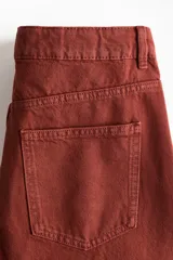 Jeans de corte baggy y tiro alto confeccionados en denim de algodón rígido, con diseño de cinco bolsillos, piernas amplias y cierre frontal con botón y cremallera.