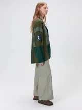 Cardigan oversize de tejido de punto grueso con diseño de bloques de color en tonos tierra. Presenta cuello en V, cierre frontal con botones, mangas largas con terminación abullonada y parches decorativos en el pecho y hombro.