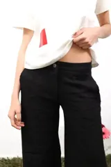 Pantalón de lino blanco de corte amplio y tiro medio-bajo. Presenta bolsillos laterales y traseros, cierre con botón metálico grabado y detalles de bordados laterales y traseros.