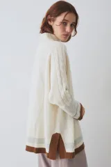 Buzo tejido de silueta amplia con cuello alto, mangas largas y puños en contraste. Presenta un diseño con franjas horizontales en el ruedo y detalles de tejido trenzado en las mangas.
