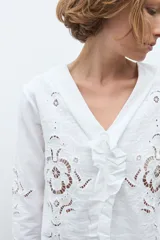 Blusa blanca de manga larga con diseño calado y bordado floral. Presenta un escote en V con detalle de volados frontales y mangas acampanadas con terminación en volado.