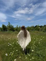 Ruana tejida en lana merino color crudo, con diseño calado, terminación en flecos y caída envolvente.