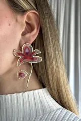 Aro individual de diseño floral con borde metálico dorado y centro en tonos rojizos y violetas, con una pequeña pieza colgante a juego.
