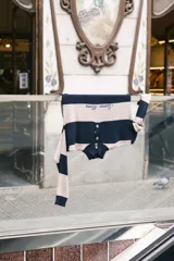 Sweater de tejido de punto a rayas horizontales anchas, alternando color azul marino y beige crudo. Presenta cuello polo con botones de guampa y bordado de la marca en el pecho.