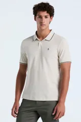 Polo de manga corta confeccionada en tejido piqué con textura tipo waffle, color beige. Presenta cuello clásico con cierre de botones y detalles de líneas en contraste en el borde del cuello y las mangas. Incluye el logo de la marca bordado en el pecho.