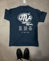 Remera azul con estampado blanco en la espalda que incluye el logo "DTLA", la frase "World Tour" y una lista de ciudades.