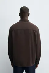 Camisa de corte regular fit confeccionada en tejido de algodón con textura de cuadrillé. Presenta cuello solapa, manga larga con puños abotonados y cierre frontal mediante botonadura.