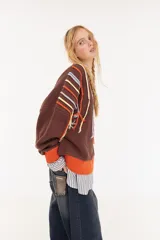 Sweater oversize de corte boxy, color crema con rayas verticales en tonos marrones y detalles de flecos colgantes. Presenta cuello redondo y puños y ruedo en tejido acanalado de color marrón oscuro.
