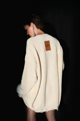 Sweater oversized color crema, tejido de punto con escote en V, roturas en ruedo y puños, y badana de PU en la espalda.