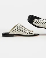 Sandalias planas blancas de cuero, con tira ancha sobre el empeine adornada con tachas plateadas.