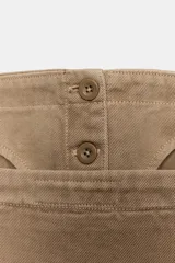 Top corto de denim color beige, con escote recto y tirantes finos ajustables. Presenta diseño con costuras verticales, cierre frontal con botones ocultos y dos bolsillos decorativos con solapa en la parte inferior.