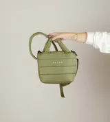 Bolsito de mano tipo puffer, color negro, con diseño acolchado horizontal y cierre superior. Presenta asas cortas acolchadas y una correa larga ajustable para llevar al hombro, con el logo de la marca estampado en el frente.