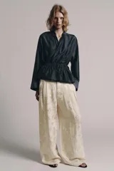 Blusa fluida cruzada de diseño envolvente, color gris oscuro satinado, con mangas largas y puños anchos. Cuenta con cuello mao y cordón ajustable en la cintura con lazada lateral.