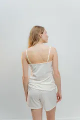 Pijama de dos piezas, compuesto por una musculosa blanca con detalle de puntilla negra elástica en el escote y un short blanco con elástico y lazo negro en la cintura.