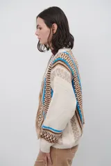 Cardigan de punto con escote en V y cierre frontal de botones. Presenta un diseño estampado con patrones geométricos en tonos beige, marrón y detalles en azul vibrante.