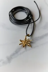 Collar con dije de acero quirúrgico en forma de flor de lirio, montado sobre un tiento de cuero encerado largo.