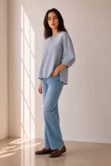 Blusa azul a rayas con bordados en el pecho, mangas tres cuartos abullonadas y cierre frontal de botones cortos.
