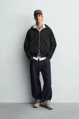 Cazadora relaxed fit color negro, confeccionada en tejido técnico ligero que repele el agua. Cuenta con cuello subido, capucha ajustable, manga larga y cierre frontal con cremallera. El interior está forrado con tejido de estructura abierta y tiene bolsillos frontales ocultos en la costura. Los acabados son elásticos.