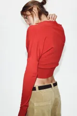 Chaqueta de punto color rojo con diseño de doble capa cruzada en el frente. Presenta cuello redondo, manga larga y cierre frontal con botones, con un acabado de tejido acanalado en el ruedo.