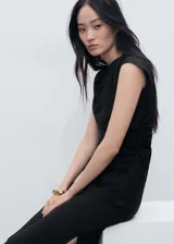 Vestido midi negro con cuello drapeado y diseño sin mangas. Presenta un corte recto con detalle de fruncido lateral en la cintura y cierre de cremallera lateral.
