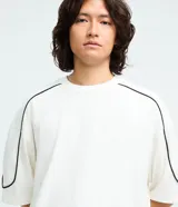 Remera de algodón color blanco, con cuello redondo, manga corta y detalle de raya negra contrastante que recorre la parte superior de los hombros y mangas. Diseño de corte holgado.