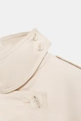 Gabardina color beige de la colección Zara Woman, con cuello solapa, manga larga y bolsillos delanteros. Presenta trabillas en los hombros, cinturón con hebilla del mismo tejido y cierre frontal cruzado con botones.