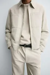 Sobrecamisa de corte regular confeccionada en tejido con estructura canvas color marrón. Presenta un ligero acolchado interior, cuello de solapa y cierre frontal con cremallera metálica. Incluye dos bolsillos de plastrón en el pecho y bolsillos laterales de vivo, con mangas largas terminadas en puños con botón.