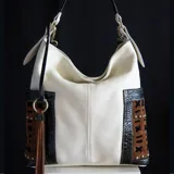 Cartera tipo hobo de cuero vacuno color arena con detalles en cuero negro texturizado y apliques de tachas. Tiene dos bolsillos laterales con diseño calado y un bolsillo trasero con cierre. Incluye correa extensible y removible para usar como morral.