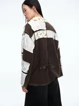 Camisa de estilo kimono con diseño patchwork, confeccionada en una combinación de tela texturizada color marrón y paneles de tela estampada con motivos florales en tonos claros. Presenta cierre frontal mediante lazo, mangas largas y bolsillos frontales.