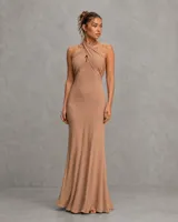 Vestido largo color tostado con escote halter cruzado y diseño drapeado que se ajusta a la silueta, de caída fluida y elegante.