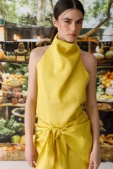 Top amarillo con cuello halter que se anuda en la nuca, dejando los hombros y la espalda parcialmente descubiertos. El tejido parece ser lino o una mezcla ligera.